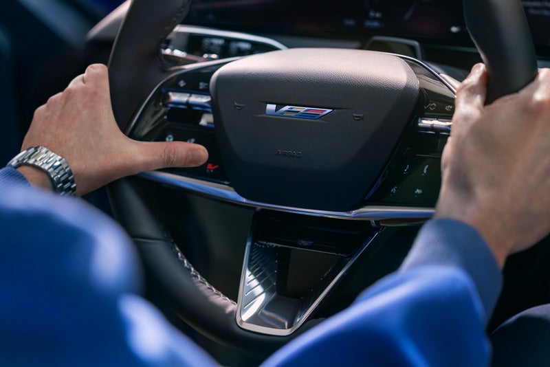 Close-up of a Man About to Press the V-Button on the 2026 OPTIQ-V Steering Wheel | Cadillac of New Orleans in Metairie LA